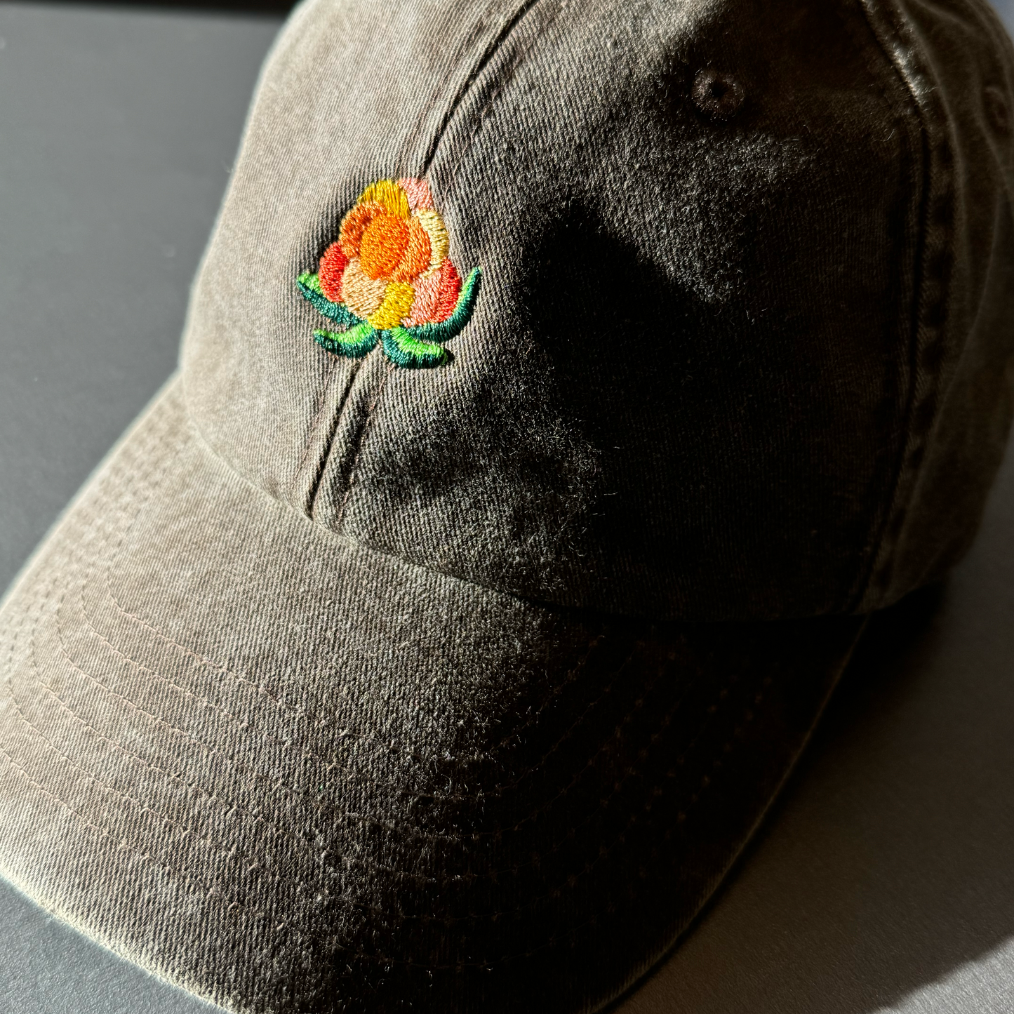 Nærbilde av broderi av multe på olivenfarget bomullscaps med vasket tekstur