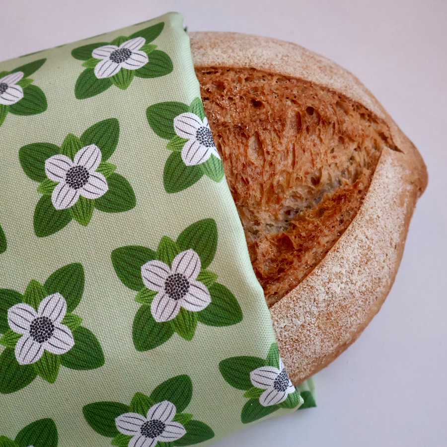 Kjøkkenhåndkle med mønster av kaffeblomst pakket rundt et nystekt brød, som viser stoffets kvalitet og dekorative bruk