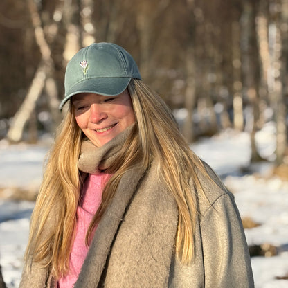 Modell med salviegrønn krokus-caps i vårsol, et friskt hodeplagg i norsk design