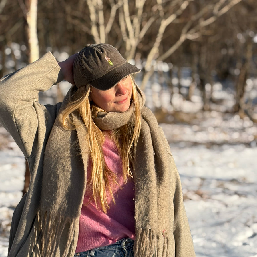 Modell med brun geitrams-caps i vinterskog, perfekt hodeplagg for tur og friluftsliv