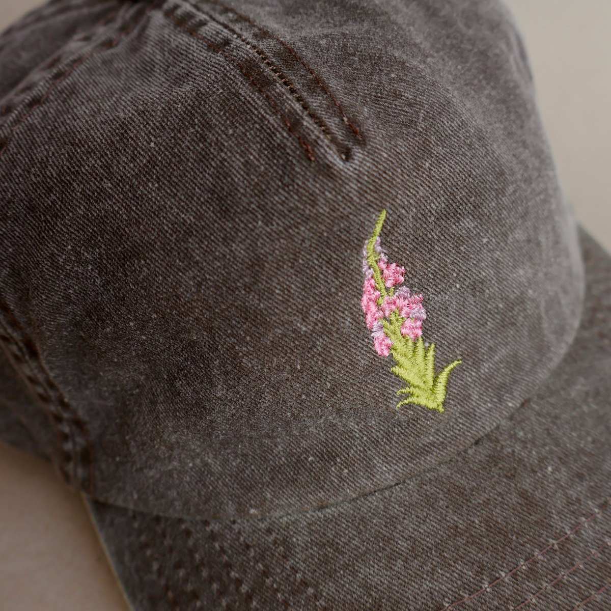 Nærbilde av detaljert geitrams-broderi på brun vasket bomullscaps, designet og brodert i Norge