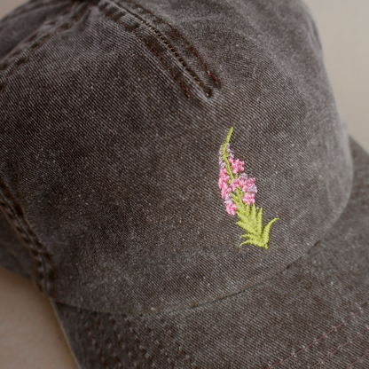 Nærbilde av detaljert geitrams-broderi på brun vasket bomullscaps, designet og brodert i Norge