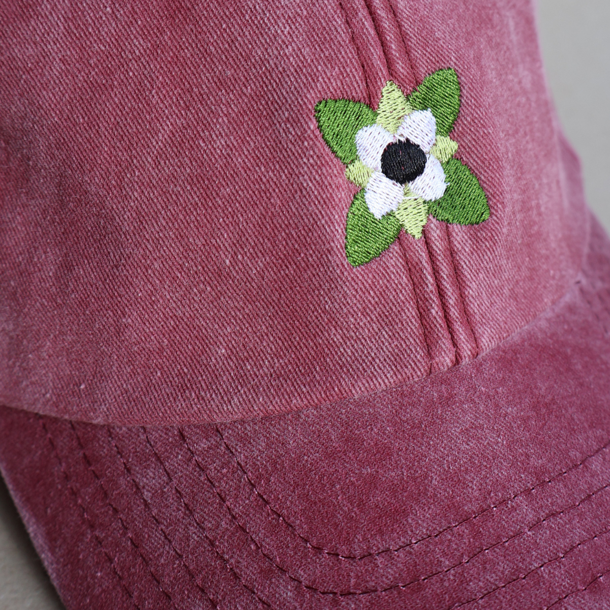 Nærbilde av hvite kaffeblomster brodert på en vinrød bomullscaps med vintage vask