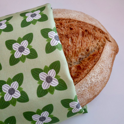 Kjøkkenhåndkle med mønster av kaffeblomst pakket rundt et nystekt brød, som viser stoffets kvalitet og dekorative bruk