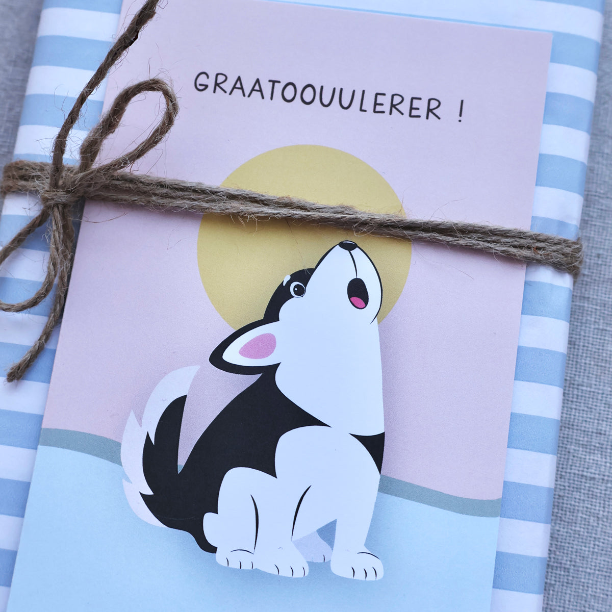 Et bursdagskort med husky-motiv festet med hyssing på en blå og hvit stripete gavepakke
