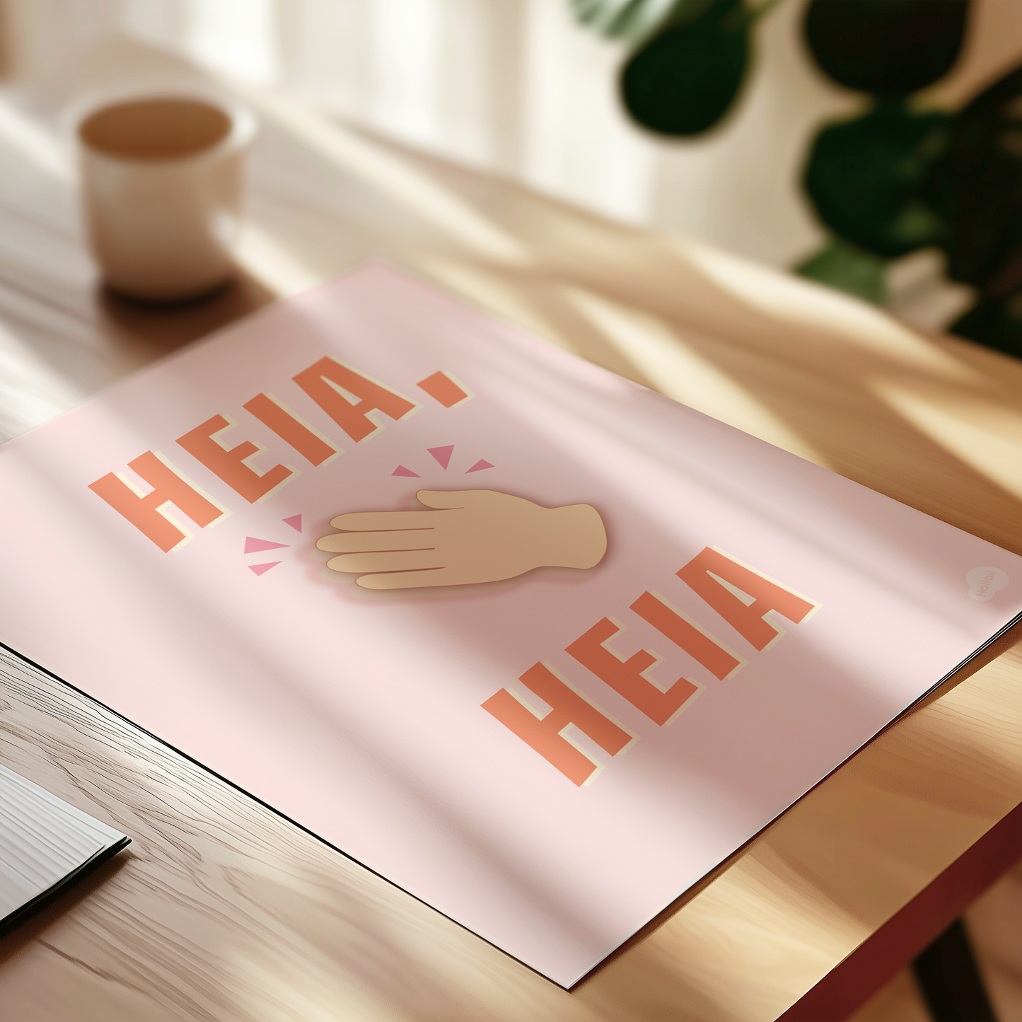 Plakat med teksten "heia, heia" og appklauderende hender, liggende på et bord med solgløtt