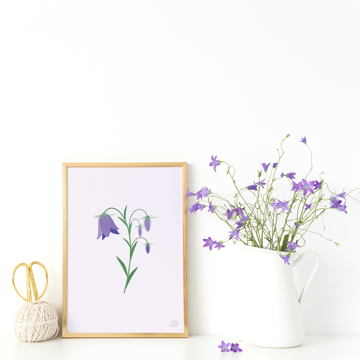 Plakat av blåklokke innrammet i ramme av tre, stående på et bord ved en vase med blomster