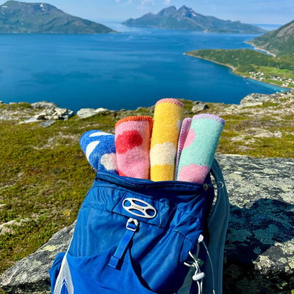 Sitteunderlag av ull, deriblant det blå kalt Godvær i serien Drømer, plassert i en sekk med utsikt til hav, fjord og himmel sett fra en fjelltopp i bakgrunnen