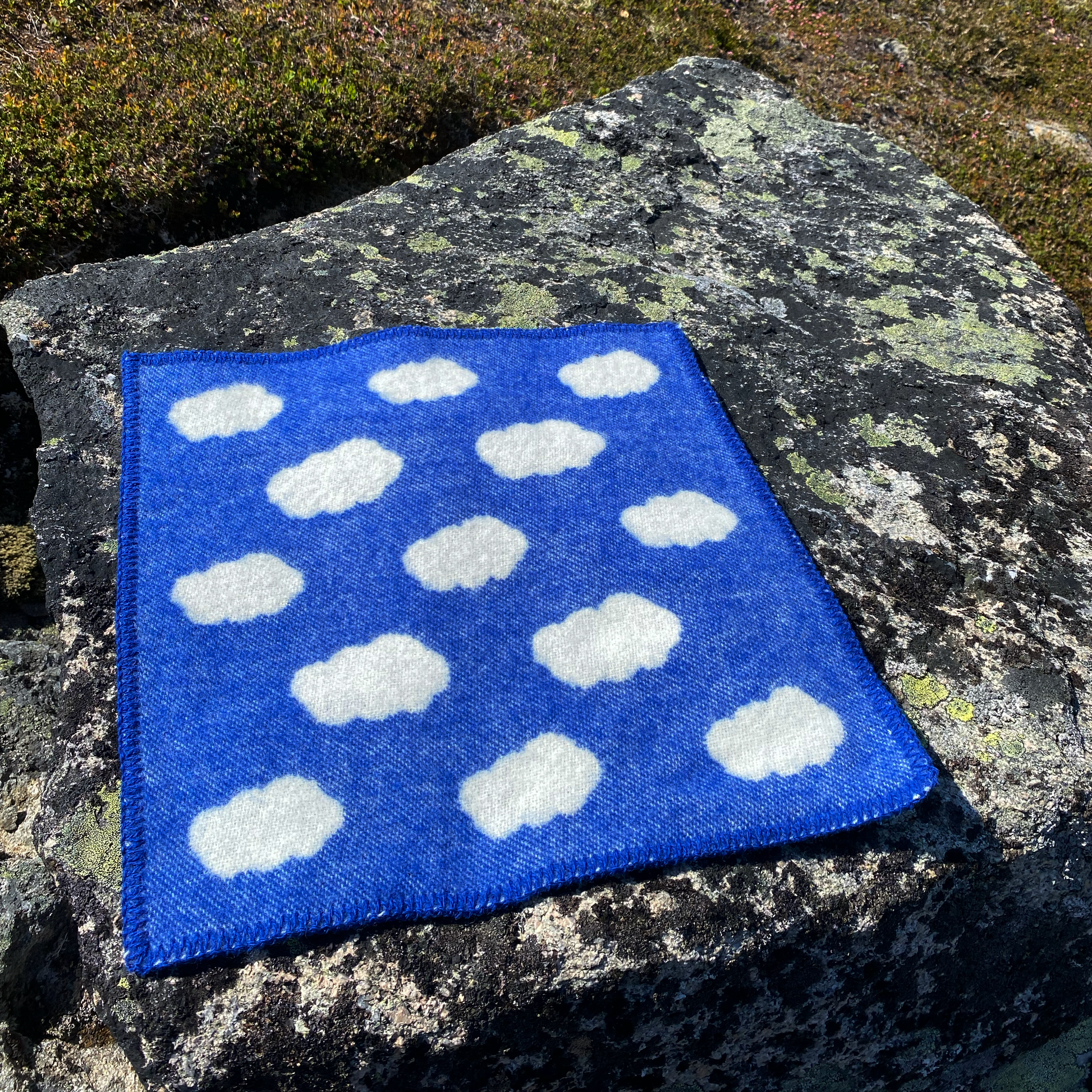 Blått og hvitt ullsitteunderlag plassert på en stein i naturen, praktisk og lunt turtilbehør i norsk design