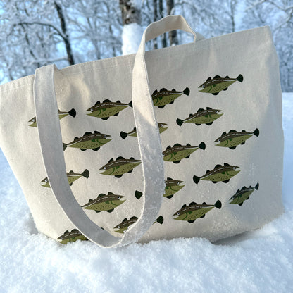 Tøyveske med brodert torsk fra Holloi stående i hvit snø, med lange bærehanker som hviler på snøen