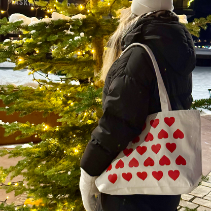Kvinne med naturfarget tøyveske med hjertemønster over skulderen, fotografert utendørs